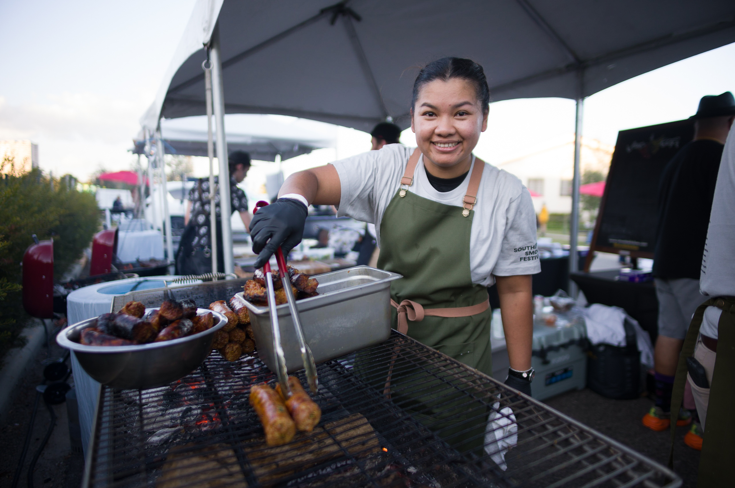 Chef Benchawan Jabthong Painter smiles while using tongs to pick up food at her booth.