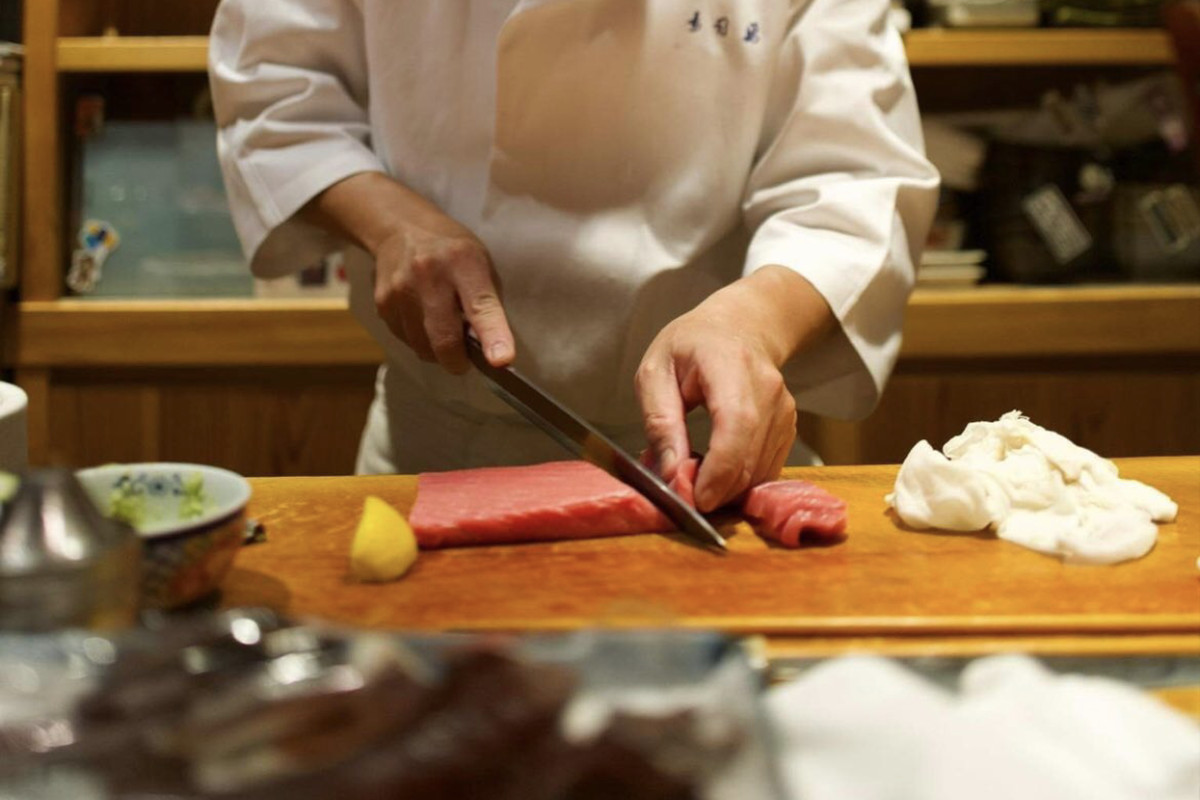 A chef slices a long piece of fish on a sushi counter.
