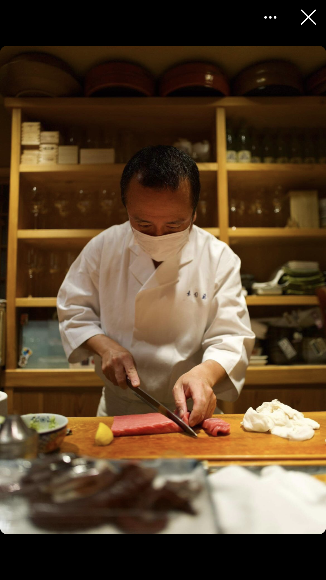 A chef slices a long piece of fish on a sushi counter.